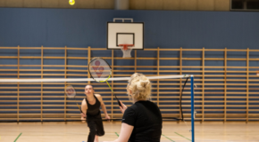 Two people playing badminton at the sports hall.