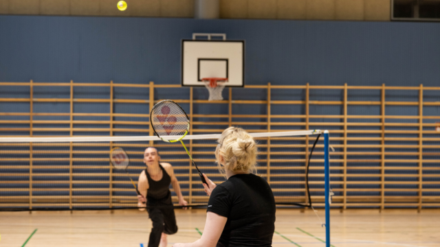 Two people playing badminton at the sports hall.